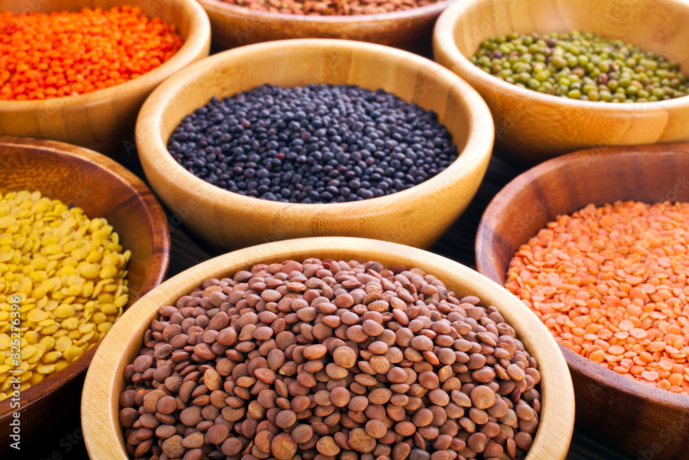 Wooden bowls of various lentils on a wooden background.