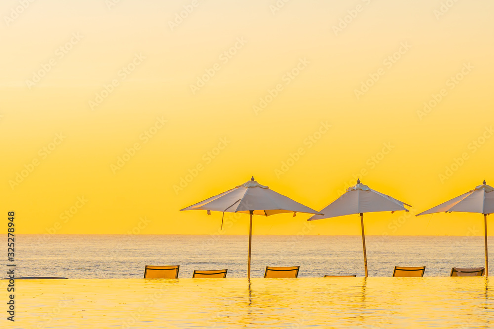 Beautiful tropical outdoor beach sea ocean with umbrella and chiar around outdoor swimming pool at sunset or sunrise time
