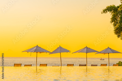Fototapeta Naklejka Na Ścianę i Meble -  Beautiful tropical outdoor beach sea ocean with umbrella and chiar around outdoor swimming pool at sunset or sunrise time