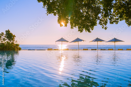 Fototapeta Naklejka Na Ścianę i Meble -  Beautiful tropical outdoor beach sea ocean with umbrella and chiar around outdoor swimming pool at sunset or sunrise time