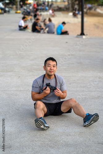 A Japanese tourist with camera sits and relaxes in t shirt and shorts near a beach in Thailand