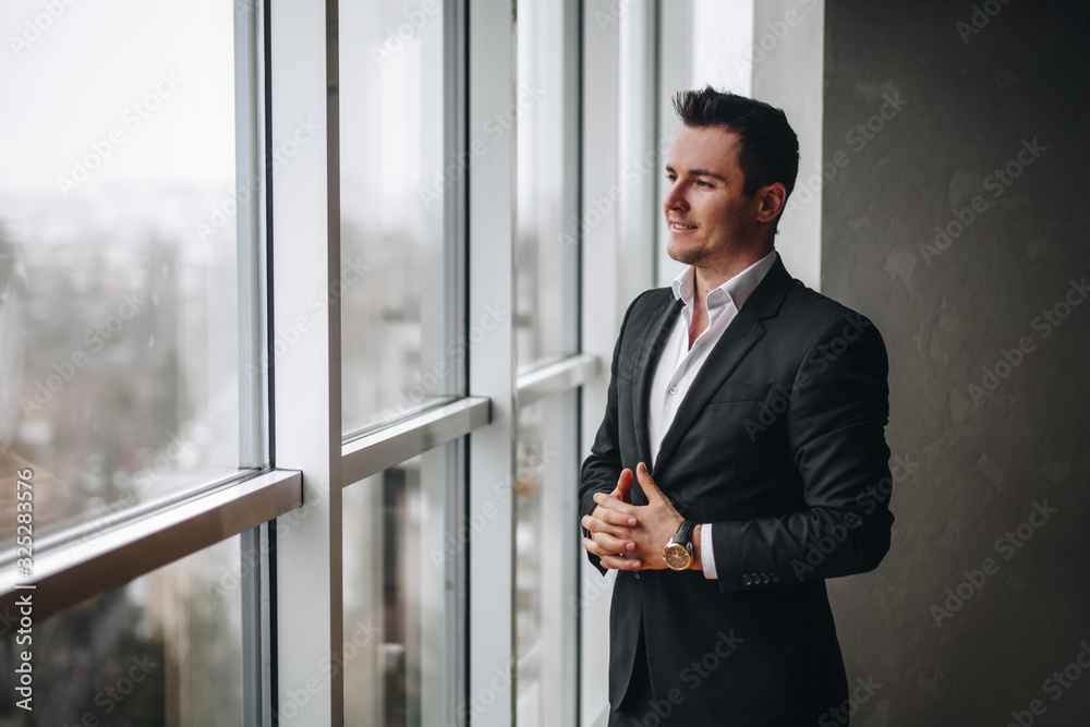 Successful and kind businessman looks out of the office window while relaxing Successful and kind businessman looks out of the office window while relaxing