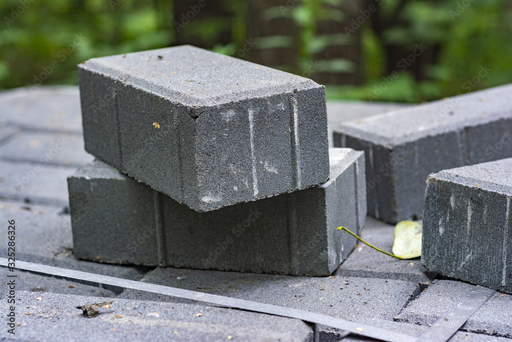 A stack of concrete bricks for laying the road in the park. Construction site on a background of green trees. A stack of concrete bricks for laying the road in the park. Construction site on a background of green trees.