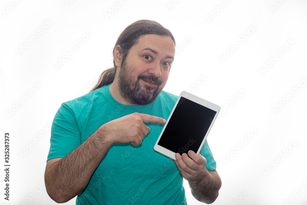 An untidily dressed and poorly shaved man holds a tablet in his hands, smiles and points a finger at him. Isolated on a white background. An untidily dressed and poorly shaved man holds a tablet in his hands, smiles and points a finger at him. Isolated on a white background.