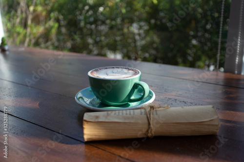 A green cup of coffee placed on a wooden table by the window in a coffee shop, Concept: Delicious breakfast drinks fragrant suitable for lifestyle, closeup cup of coffee over the top with space