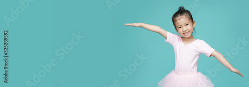 Beautiful smiling Asian little girl in a pink suit is dancing a ballet at school, empty space in studio shot isolated on colorful blue long banner background