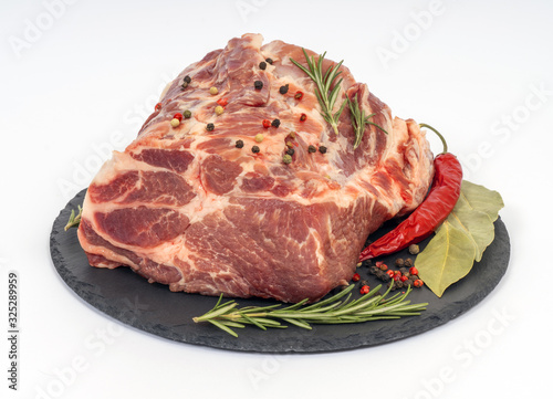 Fresh raw pork neck on black stone board isolated on white. Rosemary, pepper, bay leaf with meat. photo