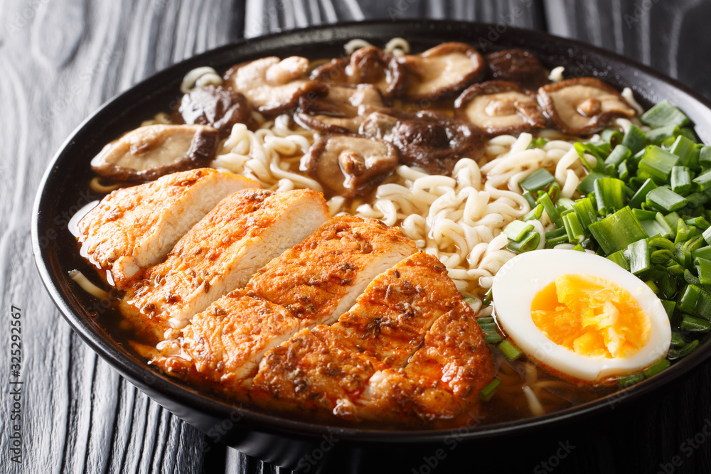 Asian style soup with ramen noodles, chicken, boiled eggs, mushrooms and green onions close-up in a bowl. horizontal