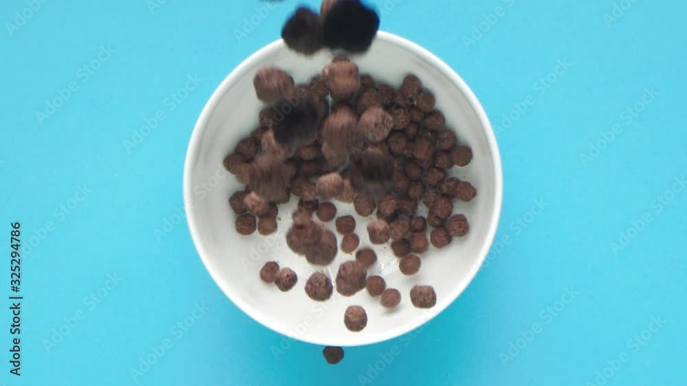 Chocolate and mouth-watering breakfast cereal balls fall into a white cup against a bright blue background Chocolate and mouth-watering breakfast cereal balls fall into a white cup against a bright blue background