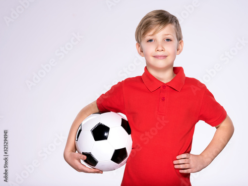 Pretty 8 years old kid in a red t-shirt with a soccer ball in hand.  Photo of a boy in sportswear holding soccer ball, posing at studio. White child holds a soccer ball. © Valua Vitaly