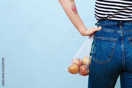 Woman with hand on her waist holding net bag with apples