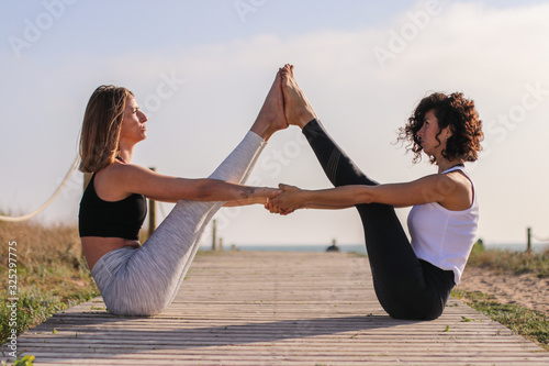 Two girls doing yoga duo outside at the beach.