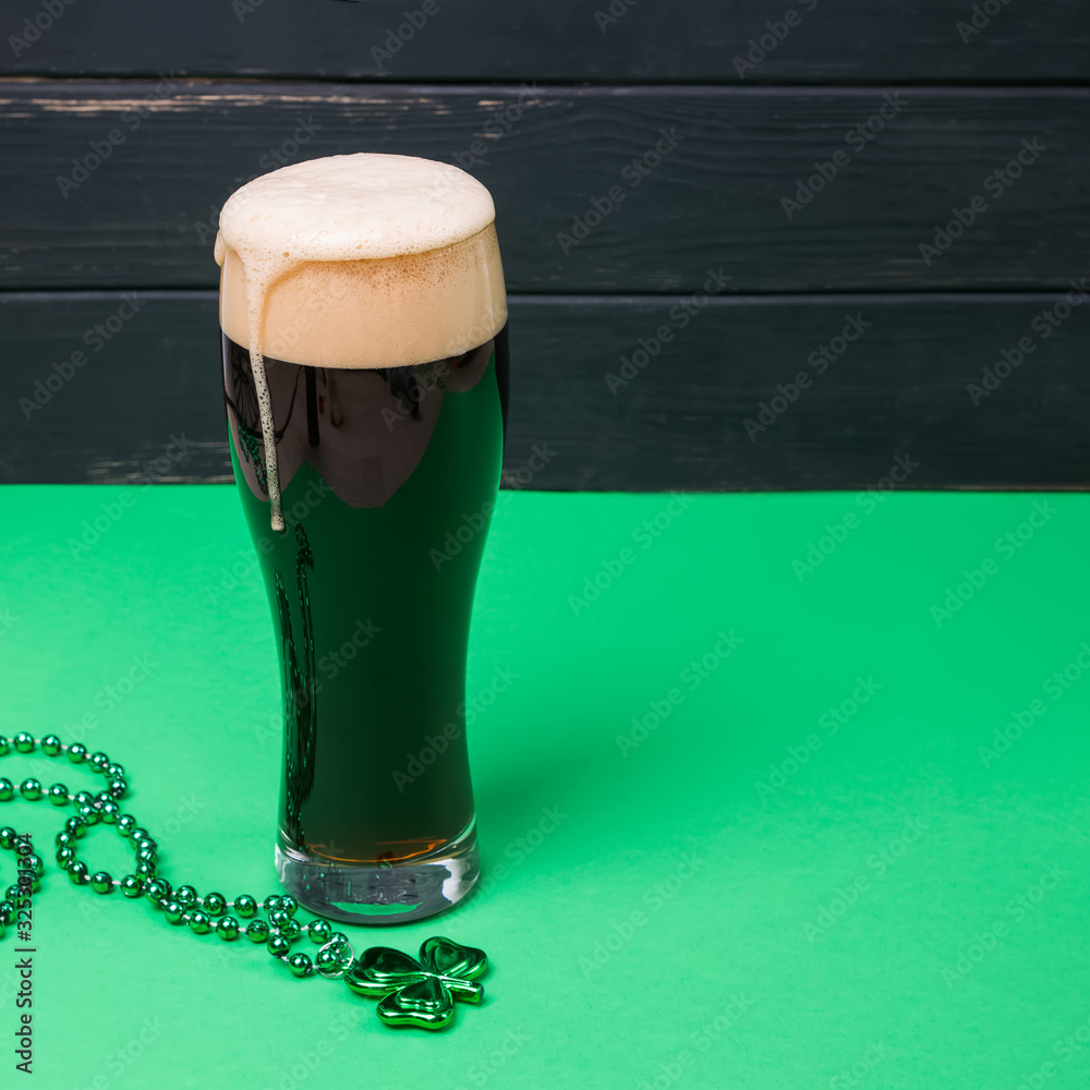 Glass of dark stout beer and traditional clover shaped decor on green table - obrazy, fototapety, plakaty 