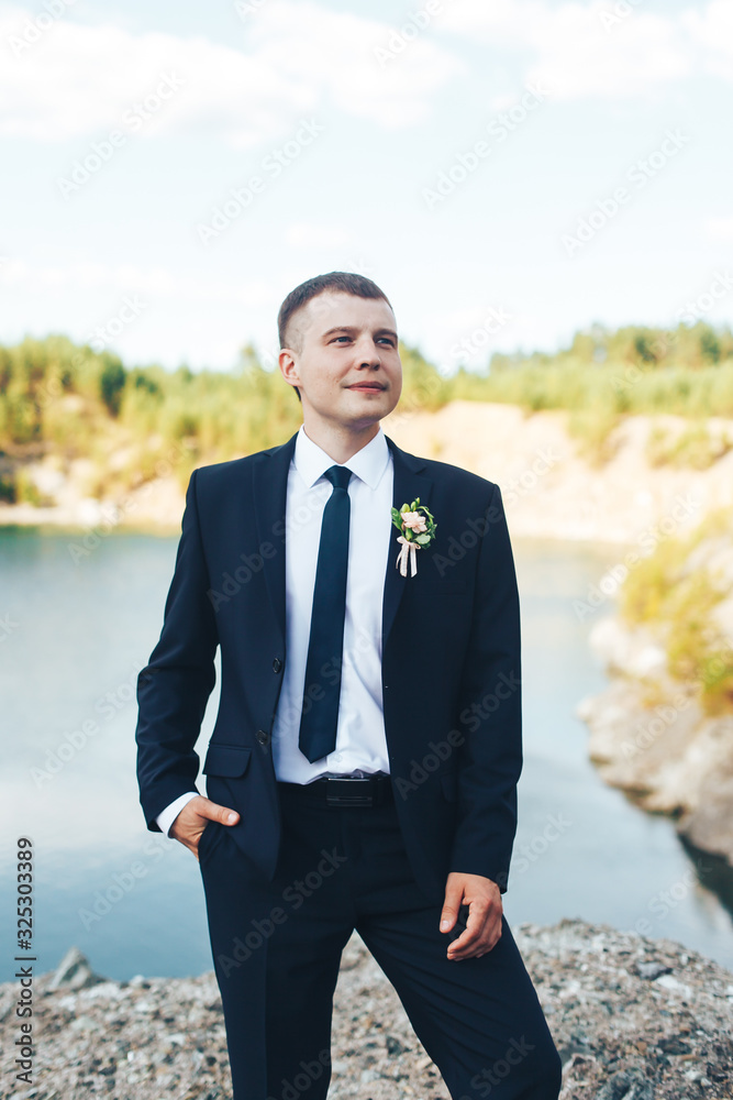 Groom stands on the lake background and smiles Groom stands on the lake background and smiles