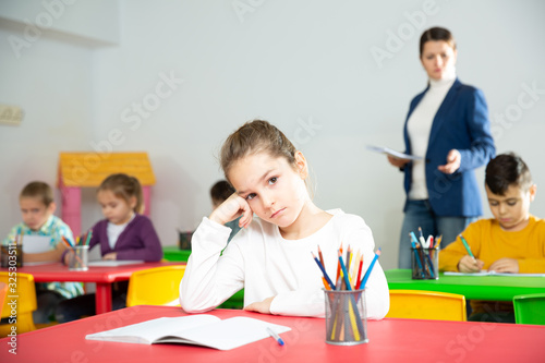 Upset schoolgirl sitting at a desk in classroom elementary school