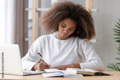 Focused african american school girl studying writing essay doing homework