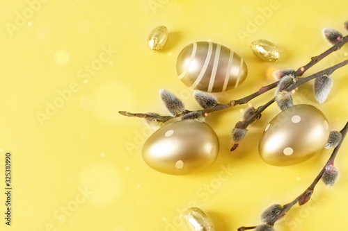 Golden colored Easter eggs and spring tree branches over yellow background. Happy Easter time.