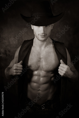 Handsome cowboy wearing hat with covered eye pulls open waistcoat to reveal defined pecs and muscular sixpack abs