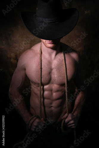 Shirtless cowboy wearing hat covering his face, holding rope around his neck with defined pecs and muscular sixpack abs