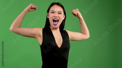 Beautiful young cheerful funny asian girl hipster shows strength for primacy and victory of will. Hands clutching portrait with bright makeup on her face.Emotions, fun, laughter and happiness.