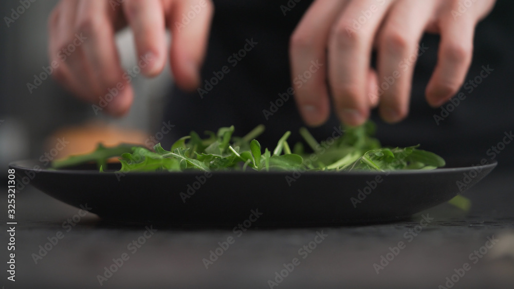 man hands arranging fresh arugula on black plate man hands arranging fresh arugula on black plate