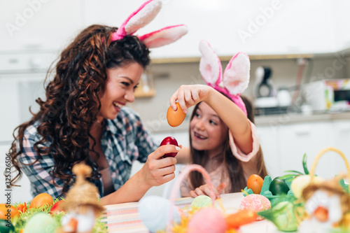A mother and her cute daughter are painting colorful eggs and wearing bunny ears. Happy family are preparing for Easter.