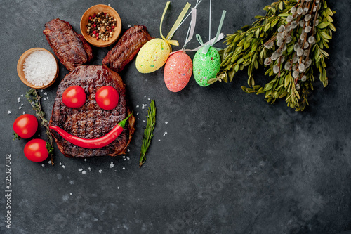Grilled festive Easter steak with spices and colorful eggs. Easter bunny on stone background with copy space for your text.