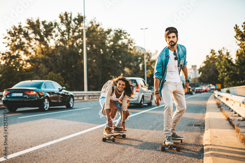 Beautiful young couple enjoying skateboarding on city street.