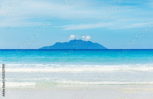 Amazing tropical beach with white untouched sand  turquoise ocean with waves and beautiful exotic island at background.Beau Vallon Beach  Mahe Island  Seychelles
