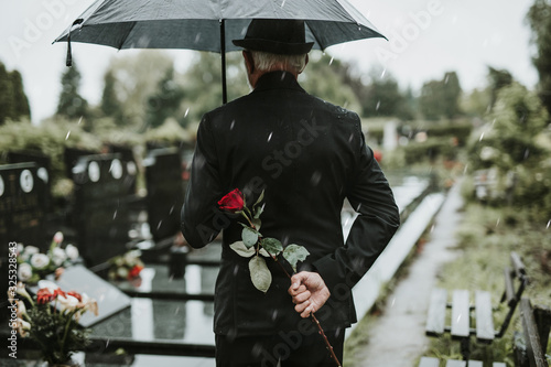 Foto Elegant sad elderly man standing on the rain with umbrella and grieves at the gr