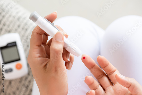 Close up of woman hands holding lancing device with blood to checking blood sugar level by Glucose meter for diabetes tester using as Medicine, glycemia, healthcare and medical concept.