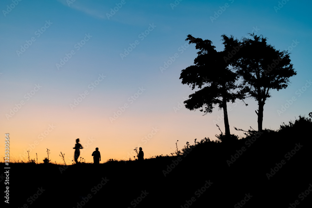 Silhouettes of people walking and running over the hill in beautiful colorful sunset. Outdoor activities