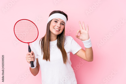 Young caucasian woman playing badminton isolated cheerful and confident showing ok gesture. © Asier