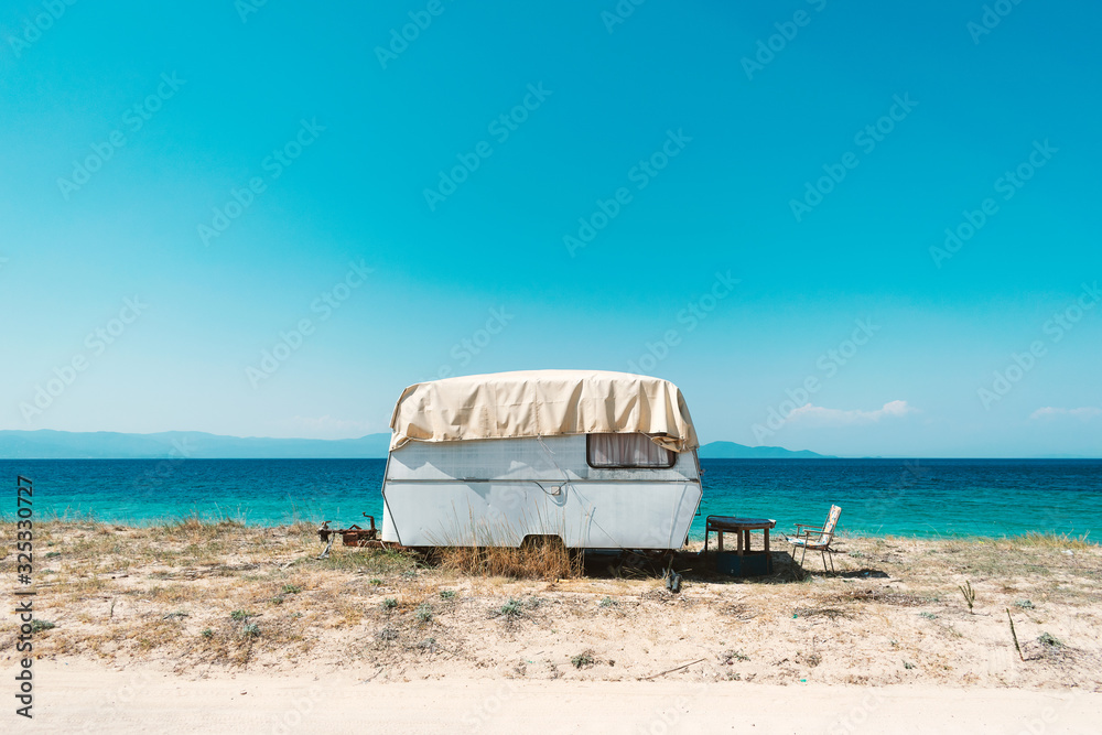 Vintage camping trailer parked on a beautiful beach. Bright warm summer day beside clear turquoise sea water. Vacation background