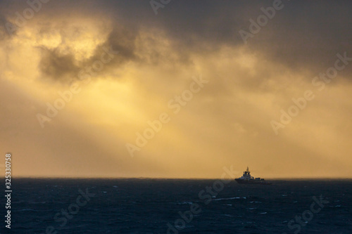 An offshore vessel in the ocean with clouds and warm sunlight.