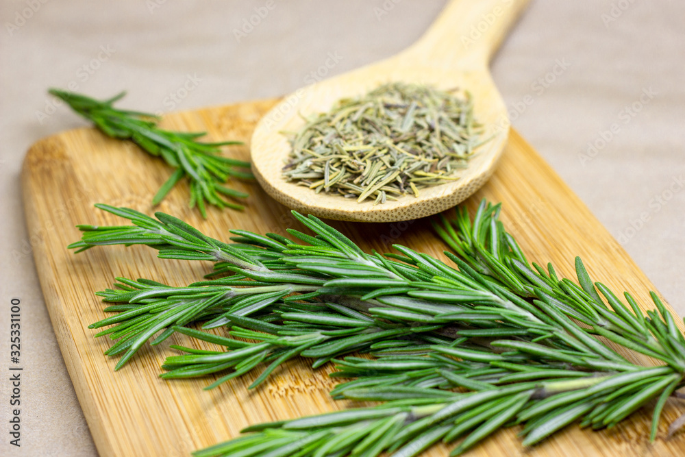 Bright fresh green and dried rosemary branches, twigs and leaves in a wooden spoon and on a board on light background. Bright fresh green and dried rosemary branches, twigs and leaves in a wooden spoon and on a board on light background.