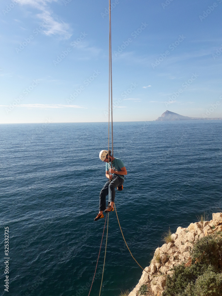 Climber in Spanish mountains hanging from a rock above the sea.