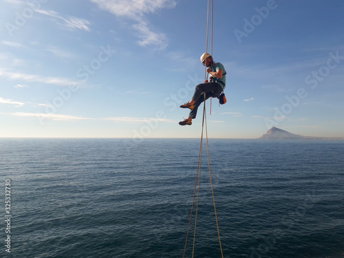Climber in Spanish mountains hanging from a rock above the sea.