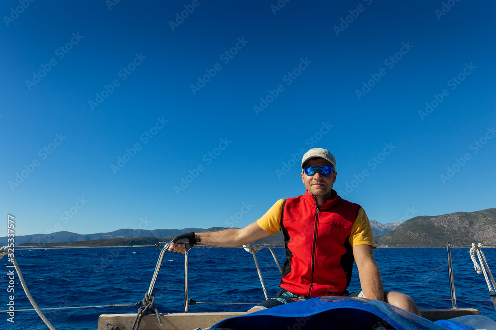 A man on a yacht sits on a deck in the background of the islands.