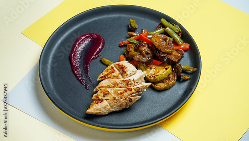 Healthy, dietary food - grilled chicken fillet with grilled vegatebles in a black ceramic plate on colored background. Close up photo