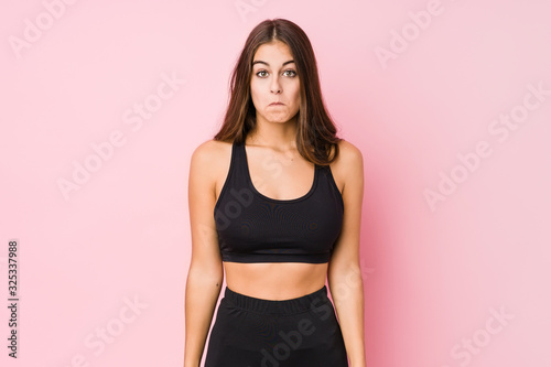 Young caucasian fitness woman doing sport isolated shrugs shoulders and open eyes confused.