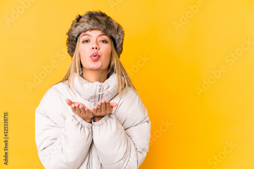 Young blonde woman wearing a winter clothes isolated Young blonde woman isolated on yellow background folding lips and holding palms to send air kiss.< mixto > photo