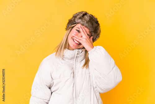 Young caucasian woman wearing a winter clothes isolated blink at the camera through fingers, embarrassed covering face.