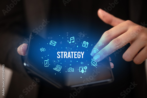 Businessman holding a foldable smartphone with STRATEGY inscription, social media concept