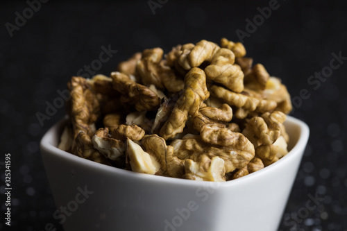 Peeled walnuts lying in a white bowl dark background warm light a healthy snack
