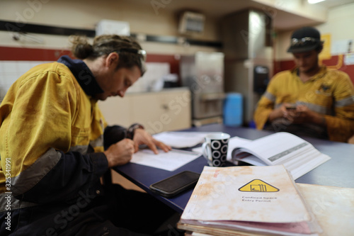 Defocused of miner seating on the chair double checking of Job hazard analysis (JSA) with JSA confined space templates forms on the table Perth, Australia
 photo