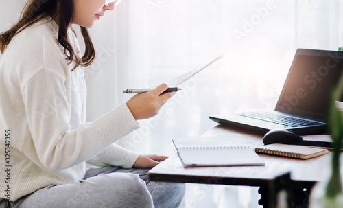 Young female holding paperwork to reading while she working with laptop in cafe