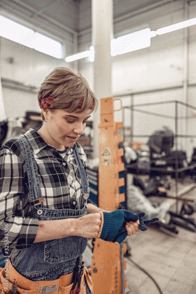 Dirty-faced female mechanic taking off protective gloves