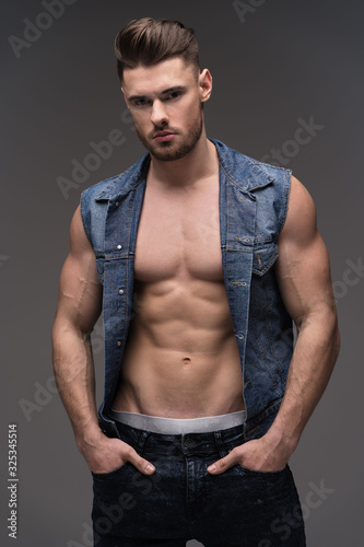 Portrait of a young man with a beard on a gray background. A muscular man in a t-shirt. Studio portrait. Fitness, fashion and beauty