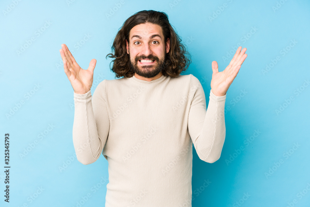 Young long hair man isolated on a blue background receiving a pleasant surprise, excited and raising hands. Young long hair man isolated on a blue background receiving a pleasant surprise, excited and raising hands.